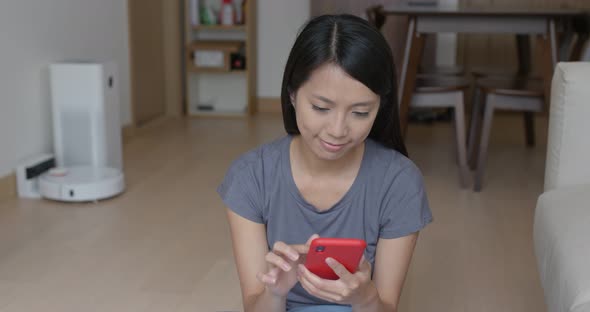 Woman control the robotic vacuum cleaner with cellphone at home