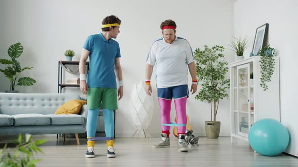 Slow Motion of Silly Guy Exercising with Stretch Band Kicking Friend Having Fun Indoors in Apartment