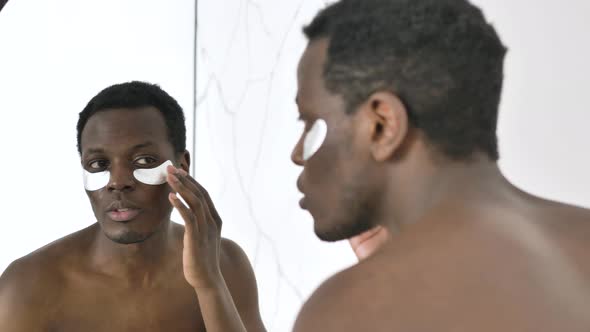 AfricanAmerican Guy with Under Eyes Patches Looks in Mirror