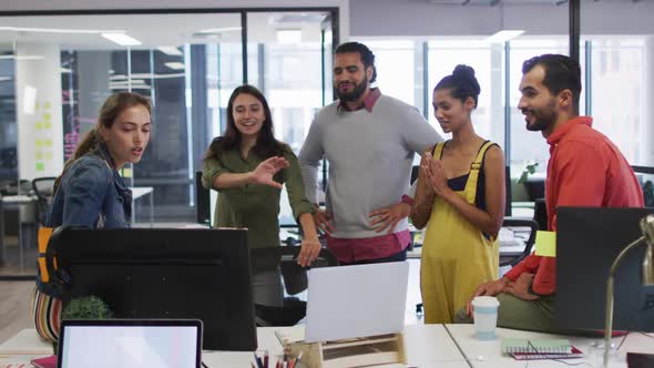 Diverse group of happy work colleagues looking at computer monitor and talking