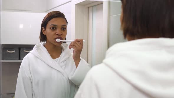 A Woman Looks in the Mirror and Brushes Her Teeth with Toothpaste a Toothbrush