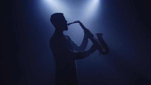 Backlit Silhouette of Saxophonist Man with Saxophone in Dark Nightclub Studio and Start Playing Sax