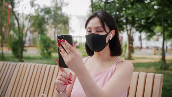 Happy mixed race girl in medical mask outdoor making video call to relatives with smartphone.