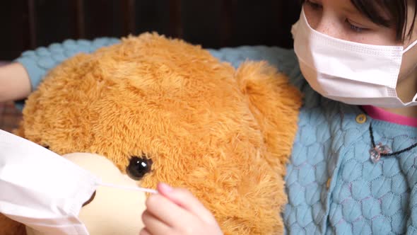 Young Caucasian girl puts mask on cute teddy bear, Covil-19 quarantine