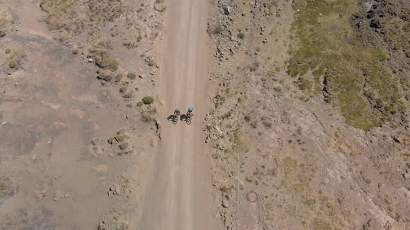 aerial shot following two mountain bikers climbing up a gravel road mountain pass
