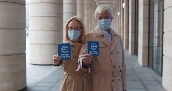 Portrait of Mature Couple in Safety Mask Looking at Camera and Showing Vaccine Passport