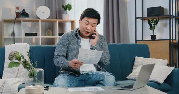 Chinese Male Worker Talking on Phone, Reading Report and Working on Laptop