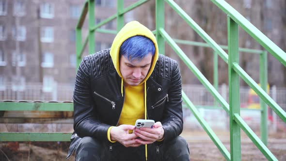 Young man with mobile phone sitting on stair on city street.