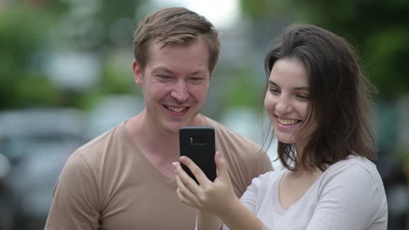 Young Happy Couple Using Phone Together in the Streets Outdoors