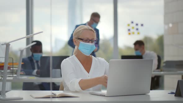 Mature Businesswoman Working on Computer in Protective Mask Sitting in Office