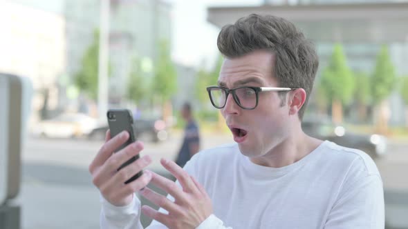 Upset Young Man Reacting to Loss on Smartphone Outdoor