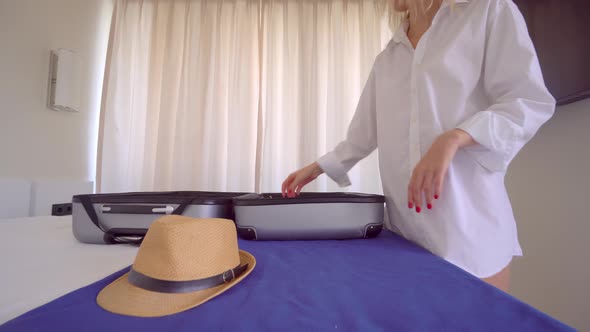 A young beautiful woman in a white shirt puts things out of a suitcase