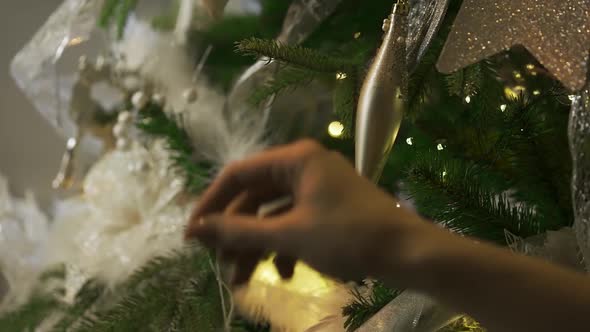 Woman Hangs a Shiny New Years Ball on a Green Fluffy Christmas Tree