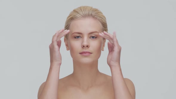 Studio portrait of young, beautiful and natural blond woman applying skin care cream. F