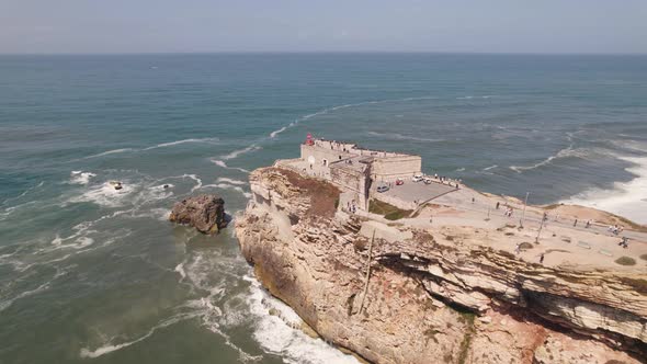 Aerial flying over clifftop Saint Michael the Archangel fort and Nazare lighthouse