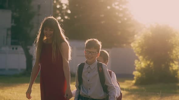 Woman in Red Dress Walks with Schoolboys in Park Slow Motion