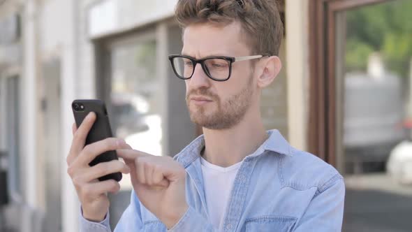 Casual Young Man Upset By Loss on Smartphone While Standing Outdoor