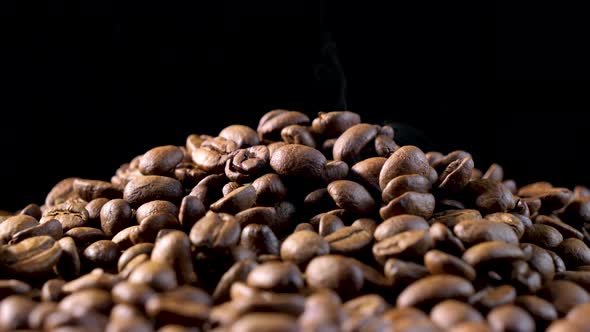 Roasted coffee beans with smoke. Slow motion of arabica coffee seeds falling.