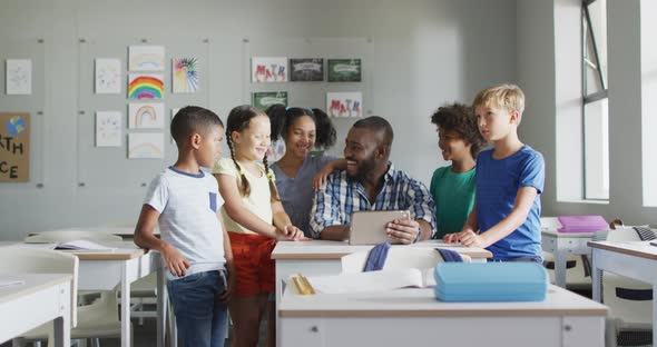 Video of happy african american male teacher and class of diverse pupils working on tablet