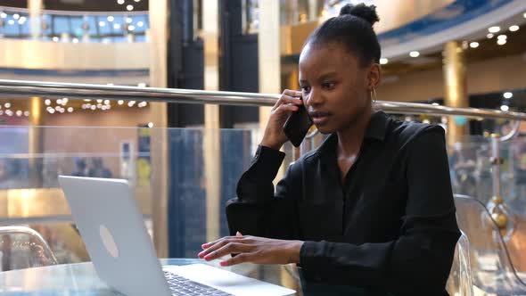 Business African Woman Talking on the Phone While Using Laptop