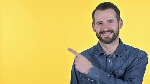 Beard Young Man Pointing at Product, Yellow Background