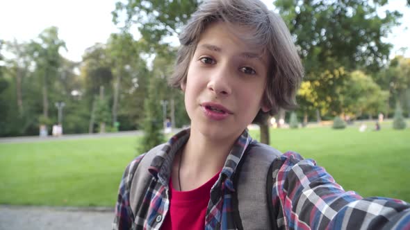 Portrait of Cute Brunette Little Boy Recording Selfie Video Outdoors. Positive Caucasian Blogger