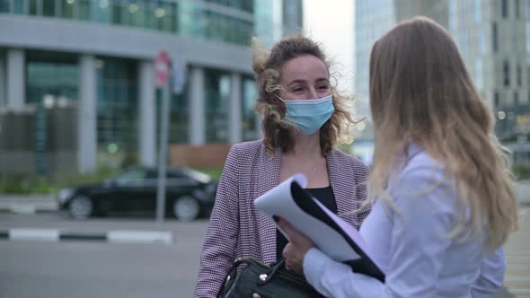 woman in medical mask talking to colleague on the street after working day