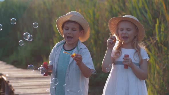 Happy Childhood, Cute Child Boy and Girl Blow Bubbles in Nature in Sunny Light