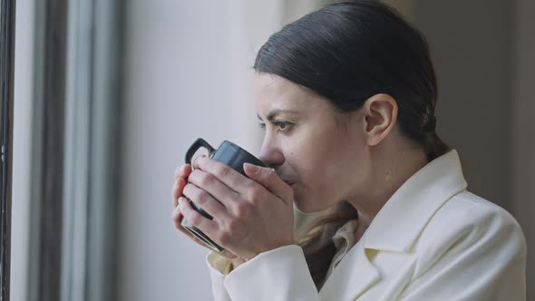 Side View Face of Relaxed Young Woman Enjoying Tea at Lunch Break Looking Out the Window