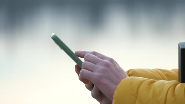 Closeup of female hands holding mobile phone browsing internet on city street.