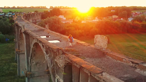 A Lady Is Crossing a Massive Stone Bridge with Sports Inventory