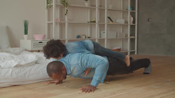 African Man Doing Push-ups with Son on His Back