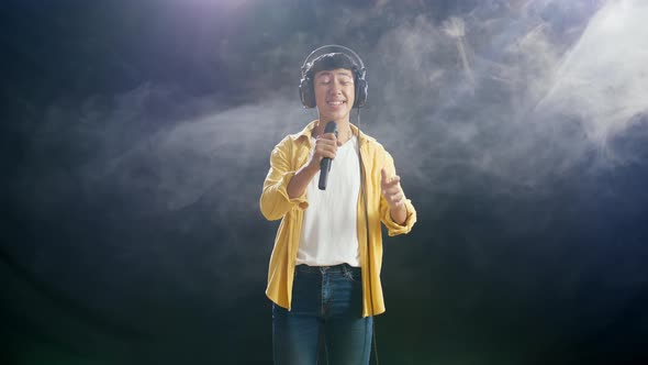 Asian Boy With Headphone Holding A Microphone And Singing On The White Smoke Black Background