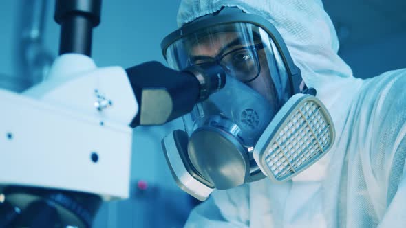 Laboratory Worker in a Hazmat Suit is Using a Microscope