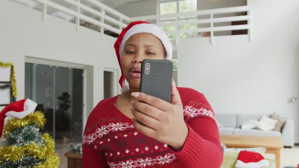 Happy african american plus size woman in santa hat, making video call on smartphone at christmas