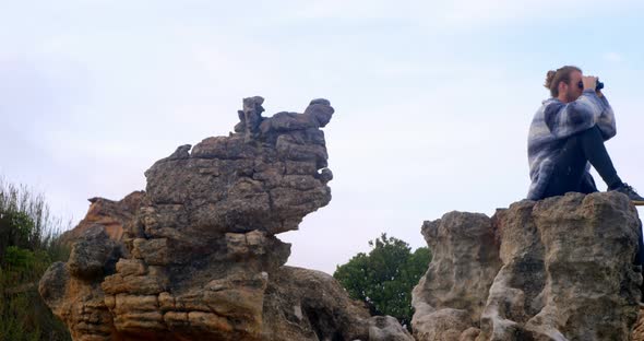 Man sitting on rock looking through binoculars 4k