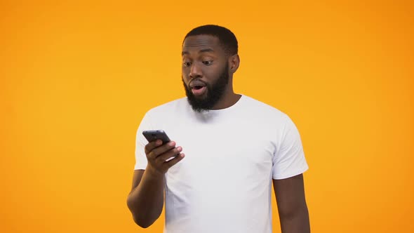 Surprised and Amazed Black Man Browsing His Smartphone Against Yellow Background