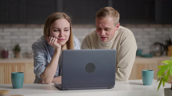 Bonding Millennial Smiling Couple Looking at Laptop Screen Choosing Goods in Online Store Involved