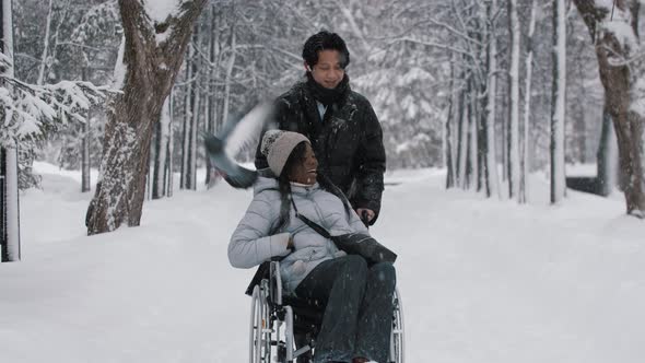 Young Couple of Asian Man and His Black Girlfriend in the Wheelchair Walking in Winter Forest