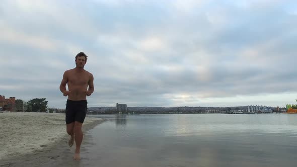 Tracking shot of a man jogging on the bay and beach.