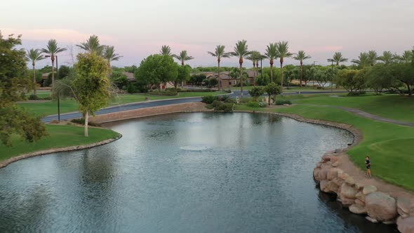 A drone retreats backwards over a golf course lake at a luxury retreat.