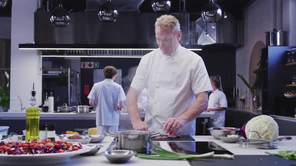 Caucasian male chef working in a restaurant kitchen, cooking and smiling at the camera