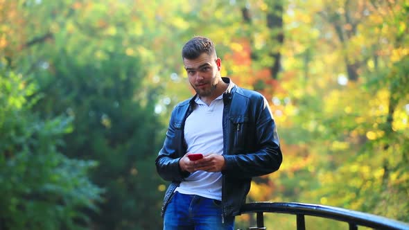 Young man with mobile phone in autumn season alley.