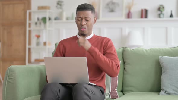 African Man with Laptop Coughing on Sofa