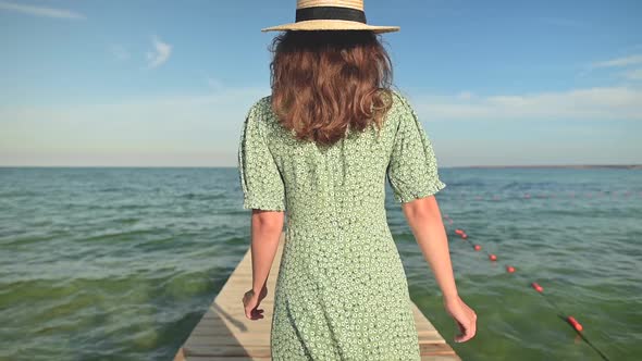 Closeup Back View Young Attractive Slender Caucasian Woman in a Green Dress and a Straw Hat Walks in