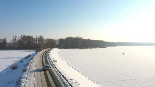 Aerial Shot of Car Riding Through Snow Covered Road Near Frozen Lake