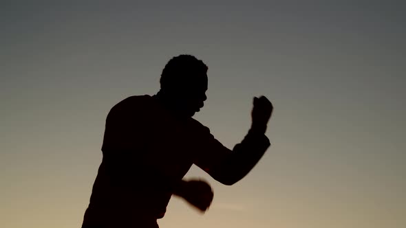 Silhouette of Africanamerican Man Training to Boxing Outdoors Against Background Sky Side View