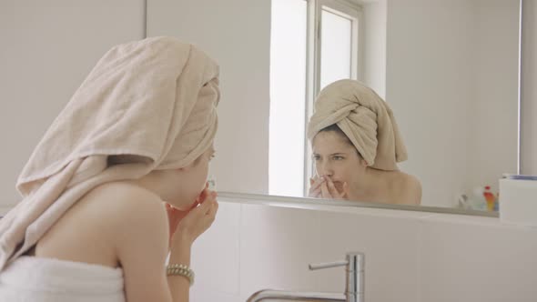 Teenage girl looking at the mirror in the bathroom - checking her face