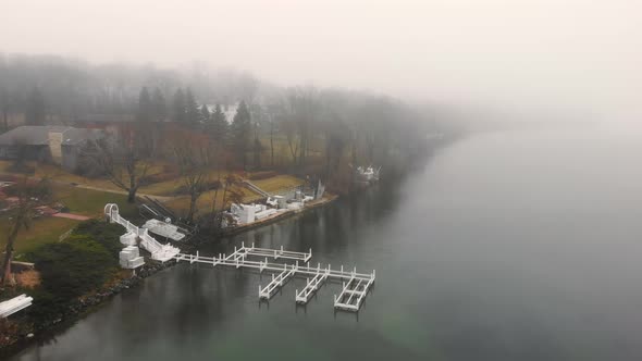 Aerial Flying Over the Lake in Heavy Fog and Cloudy Weather. The Embankment of the Lake on a Foggy