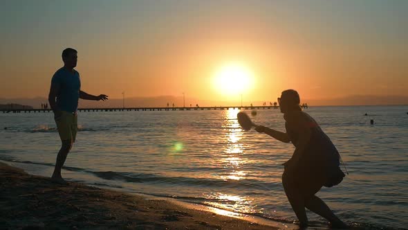 Couple playing tennis on the beach at sunset